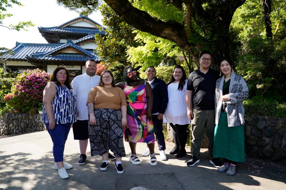 Group photo of eight people standing outside a Japanese-style building.
