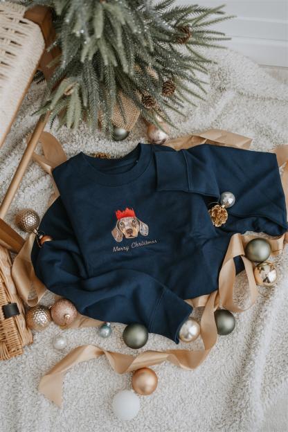 Navy blue sweatshirt with a printed dog wearing a crown and "Merry Christmas" text, surrounded by Christmas ornaments and ribbon.