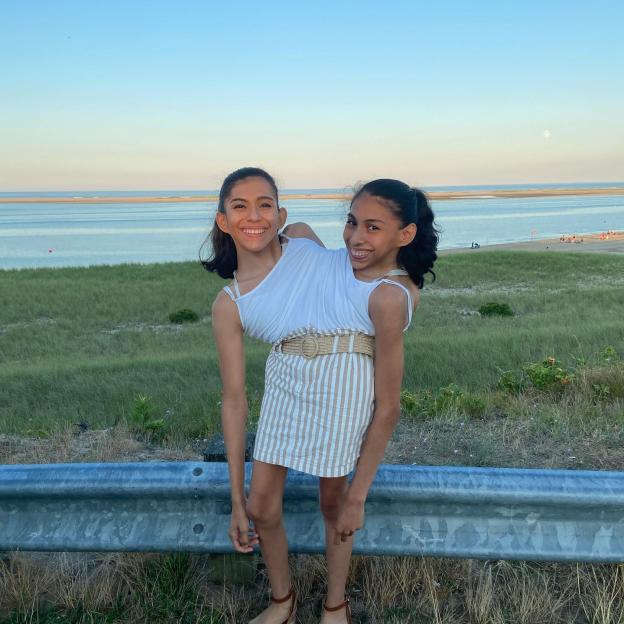 Conjoined twins Carmen and Lupita Andrade standing on a roadside overlooking a beach and ocean.