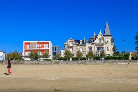 Person walking on a sandy beach with buildings in the background.