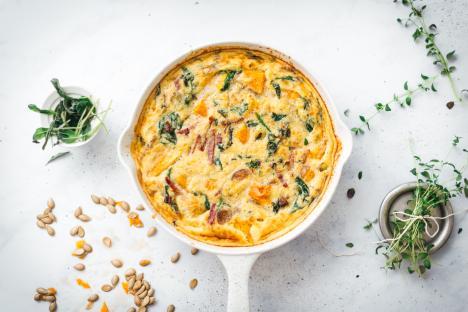 Paleo frittata with spinach and squash in a white skillet.