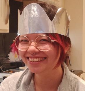 Photo of a smiling young woman wearing glasses and a paper crown.