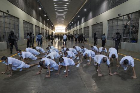 Prisoners in white uniforms exercising in a cellblock under the supervision of prison officers.