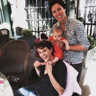 Two women and a baby sitting outdoors.