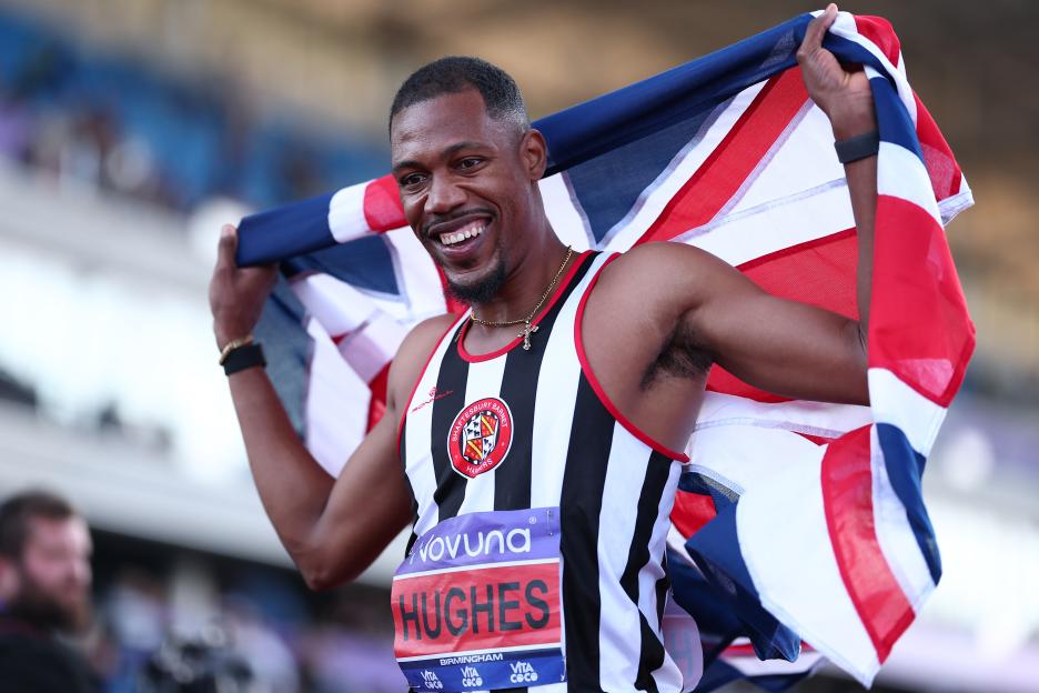 Zharnel Hughes celebrating a win, holding a UK flag.