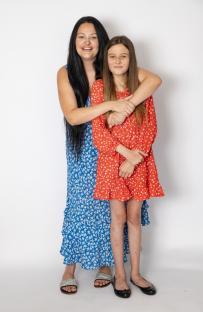 A mother and daughter in floral dresses hugging.