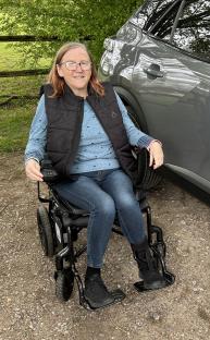Woman in wheelchair next to car.