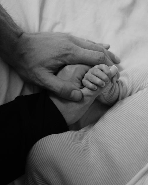 Black and white photo of Kai Havertz and his wife holding their newborn baby's hand.