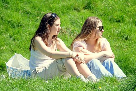 Two women sitting in a grassy park on a sunny day.
