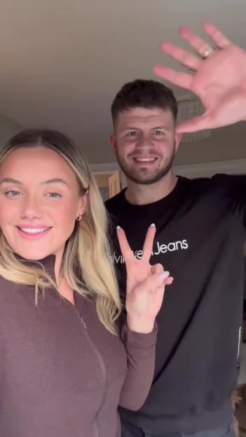 A blonde woman and a dark-haired man smiling at the camera, the woman making a peace sign and the man holding up his open hand.