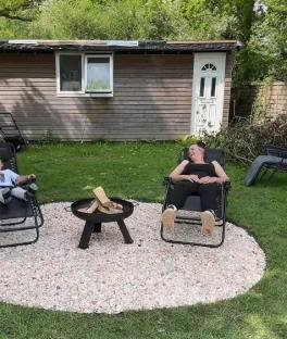 Two people relaxing in lawn chairs around a fire pit in a backyard.