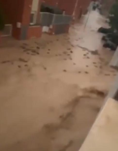 A street is flooded with brown, muddy water, reaching several feet high and covering parts of buildings.