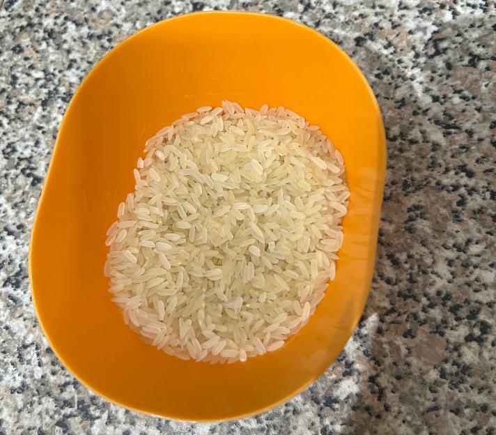 An orange scoop full of uncooked white rice on a speckled counter.