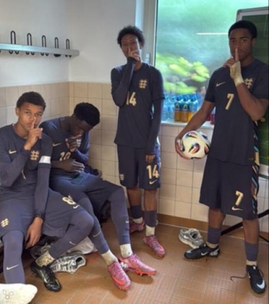 Four young soccer players in uniform, sitting in a locker room.