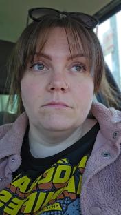 Close-up of a woman with bangs wearing a pink jacket and a graphic t-shirt.