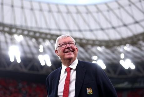 Sir Alex Ferguson smiling at a stadium.