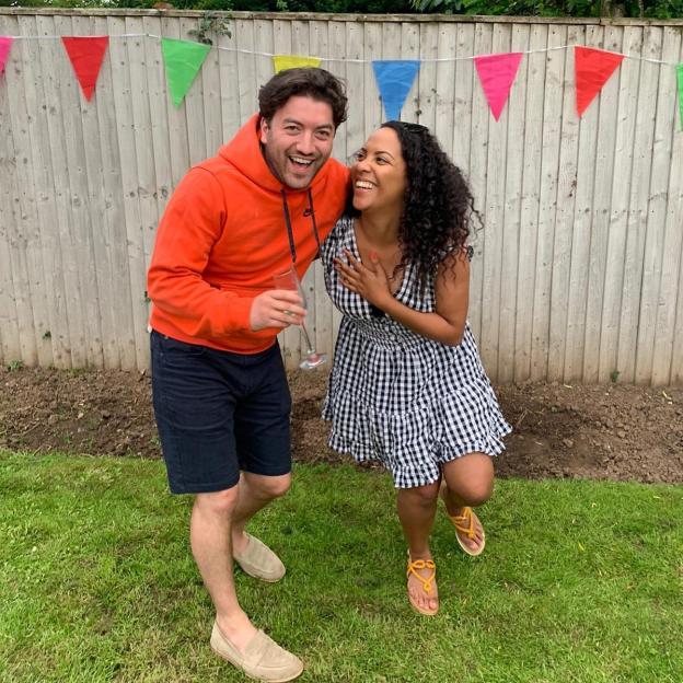 Johnny Clark and a woman laughing together at a garden party.