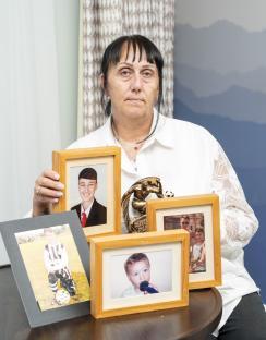 A woman sits holding framed photos of her son and a trophy.