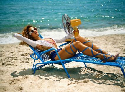 Woman relaxing on a blue beach chair with a small fan.