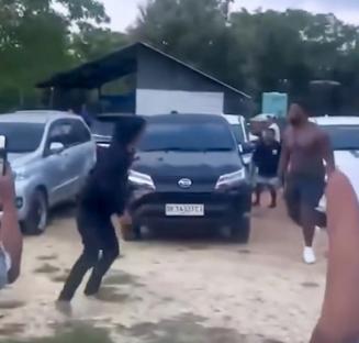A man running away from a fight near cars.