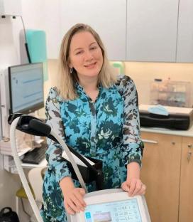 Woman in teal floral dress operating cosmetic treatment machine.