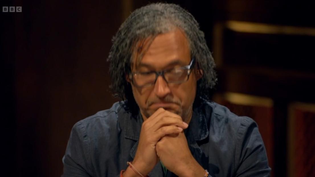 Man with gray hair and glasses with his hands clasped under his chin.