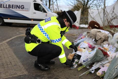Police officer placing a card among flowers and stuffed animals left as tributes.