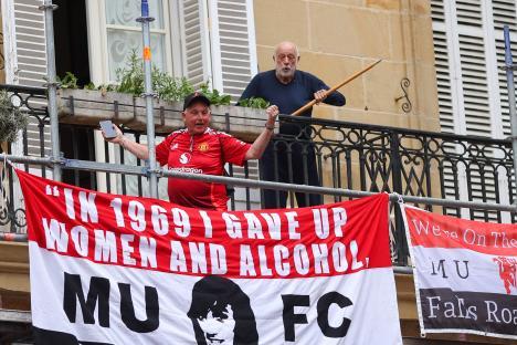A Manchester United fan on a balcony holds a banner that reads,