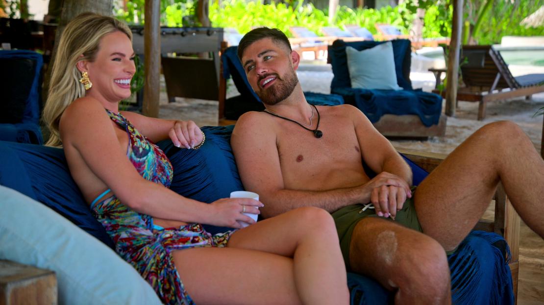 A man and woman sitting together on an outdoor couch, smiling and talking.