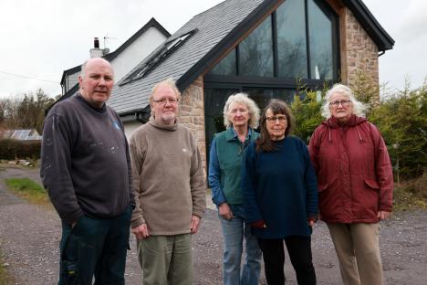 Five neighbors stand in front of a newly built house, expressing their anger about it lacking planning permission.