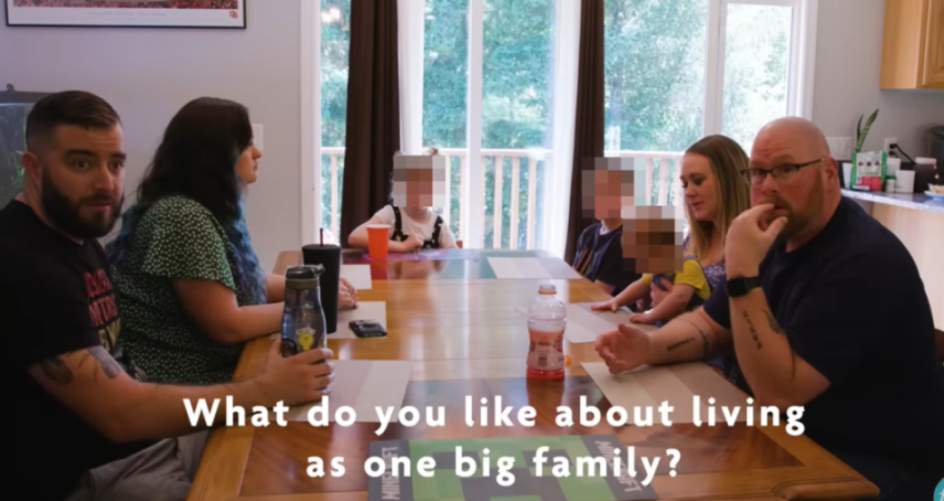 Two men, two women, and four children sit around a table.