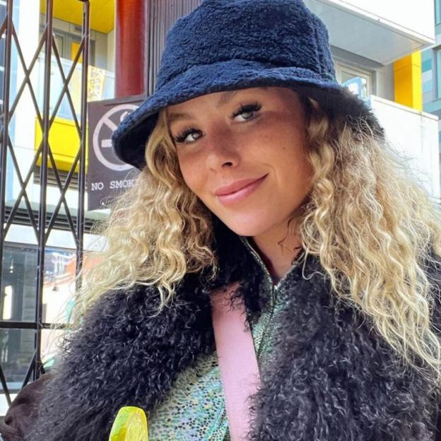 Anna-Jo Charles smiles at the camera while wearing a bucket hat and a faux fur jacket.