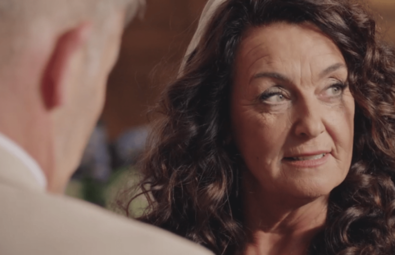 A woman with dark curly hair looks intently at a man whose back is to the camera.
