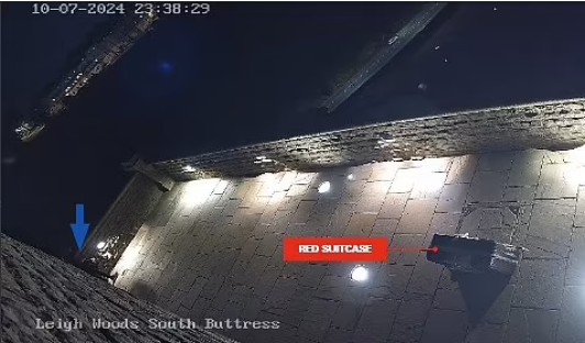 Nighttime security camera image of a red suitcase on a patio.