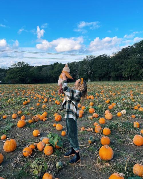 Woman holding a baby up in a pumpkin patch.