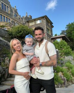 Pregnant woman, man, and toddler in front of a stone building.
