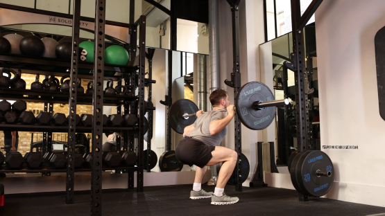 Man performing barbell back squats in a gym.