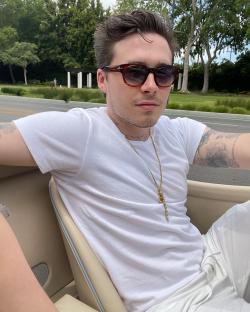 Brooklyn Beckham wearing sunglasses and a white shirt in a car.