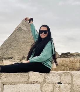 Woman sitting on a low wall in front of a pyramid.