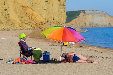 Sunbathers relaxing on a beach under a rainbow umbrella.