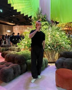 Man drinking from a glass in front of a large floral arrangement.