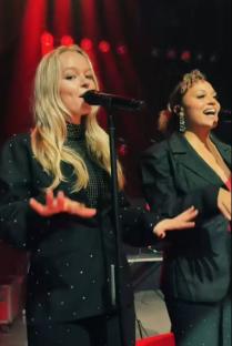 Two women singing into microphones on stage.