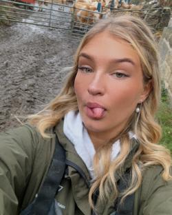 Woman sticking out tongue near cows in a muddy pen.