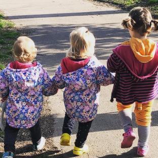 Three toddlers walking hand-in-hand down a path.