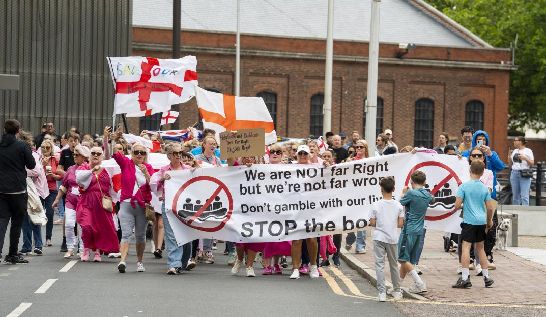 Protestors outside the Britannia Hotel in Canary Wharf holding signs and flags.
