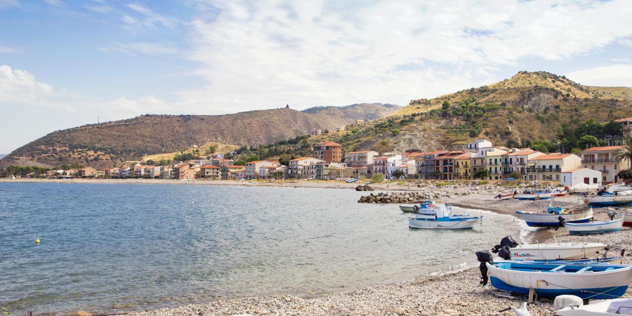 Castel di Tusa, Sicily harbor with boats on a pebble beach.