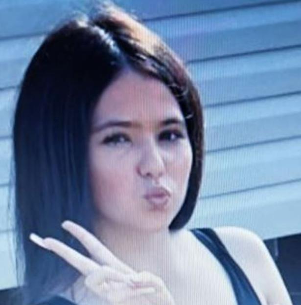 Headshot of a young woman with dark hair making a kissy face and peace sign.