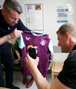 Two men looking at and photographing a West Ham United jersey.