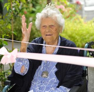 115-year-old woman wearing a tiara and waving.