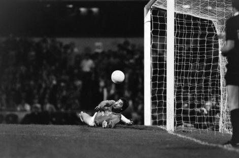 Black and white photo of a soccer goalie diving for the ball in front of the goal.